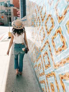 a woman walking down the sidewalk next to a wall with colorful tiles on it's side