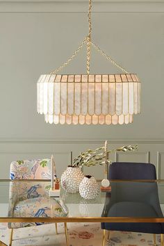 a chandelier hanging over a dining room table with chairs and pillows on it