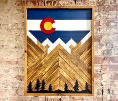 a wooden frame hanging on a brick wall with the flag of colorado painted on it