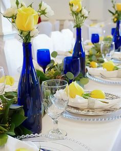 the table is set with blue vases and yellow roses in them, along with other place settings