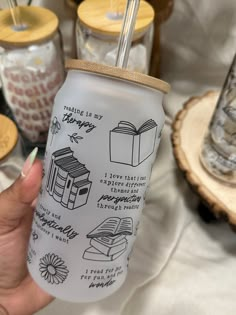 a hand holding a mason jar with different things drawn on it and straws in the background