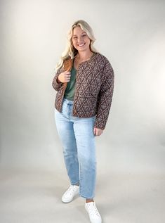 a woman standing in front of a white background wearing jeans and a cardigan sweater