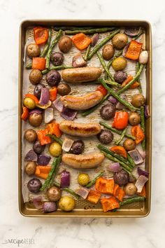 a pan filled with vegetables and meats on top of a marble countertop next to a wooden spatula