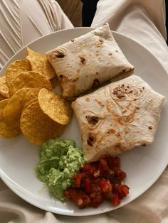 a white plate topped with tortilla and guacamole next to chips