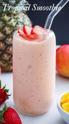 a smoothie in a glass with strawberries and pineapples on the side