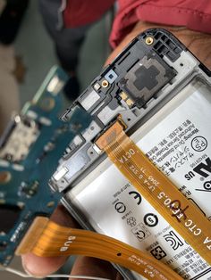 a person holding a yellow ribbon attached to the side of a cell phone that is being dismantled