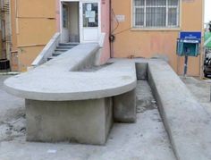 a concrete bench sitting in front of a building with stairs leading up to the door