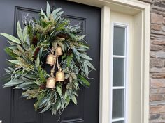 a wreath is hanging on the front door with bells and greenery as well as pine cones