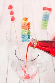 someone is pouring something into a glass with candy lollipops on sticks in it