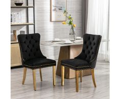 a pair of black velvet dining chairs with gold legs and studded trimmings