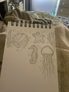 a notepad with drawings of sea animals and seashells on it sitting on a bed