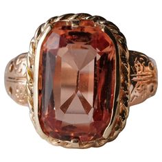 This is a genuinely impressive and rather spectacular ring. It features a large, cushion-cut reddish-orange precious topaz that has been certified natural, untreated and with a Brazilian origin. Brazil is the most desirable location for fine topaz. The interesting thing about topaz is that it's extremely common; almost all of it is colorless and then treated with heat or irradiation to alter the color. But there's another variety of topaz -imperial or precious topaz- that which derives its color Imperial Topaz Ring, Precious Rings, Imperial Topaz, Reddish Orange, Ring Antique, Gold Halo, Jade Ring, Rare Gemstones, Topaz Stone