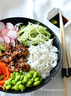 a plate filled with rice, meat and veggies next to chopsticks