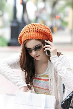 a woman is talking on her cell phone while holding shopping bags and wearing a knitted hat