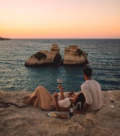 two people sitting on the beach drinking wine