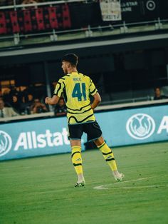 a soccer player in yellow and black is on the field with his foot off the ground