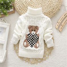 a sweater with a teddy bear on it and other items around the neck, sitting on a table