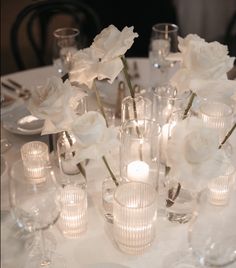 a white table topped with lots of glass vases filled with flowers and lit candles