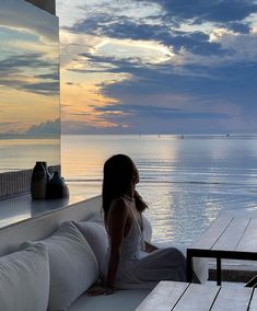 a woman sitting on top of a white couch next to the ocean