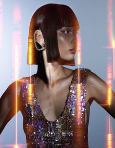 a woman with short hair and earrings standing in front of an image of neon lights