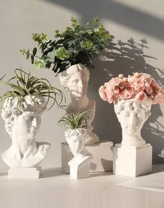 three white vases with flowers and plants in them on top of a table next to a wall