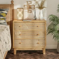 a bedroom scene with focus on the dresser and bed in the foreground, there is a potted plant next to it