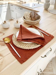 a wooden table topped with plates and bowls next to a basket filled with bread on top of it