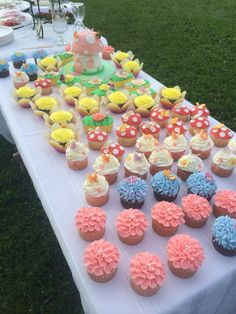 a table topped with lots of cupcakes on top of a white table cloth