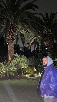 a man standing in the middle of a park at night with palm trees behind him