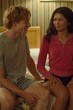 a man and woman sitting on top of a bed next to each other in a bedroom