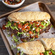 two hamburgers with lettuce, tomatoes and onions on a tray next to a bowl of salsa