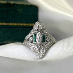 a close up of a diamond and emerald ring on a white cloth with a book in the background