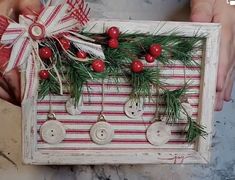 two hands holding a wooden box with buttons and pine needles on it, decorated with red berries