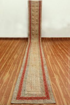 an old rug is laying on the floor in front of a white wall and wooden floors