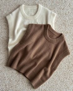 two sweaters laying on the floor next to each other, one in white and one in brown