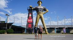 two women standing in front of a giant statue of a man holding a coca - cola bottle