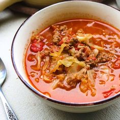 a bowl of soup with meat and vegetables in it next to a spoon on a table