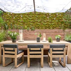 a wooden table with four black chairs and plants on it in front of a brick wall