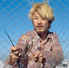 a man standing behind a chain link fence with scissors in his hand and looking at the camera