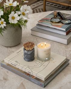 a candle and some books on a table with flowers in a vase next to it