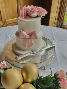 a three tiered cake with pink flowers on top and gold eggs around the base