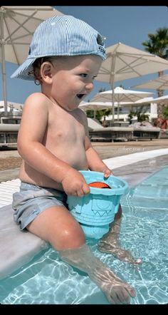 a baby sitting in the pool playing with a bucket