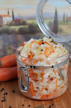 carrots and cabbage in a glass container on a wooden table next to other vegetables