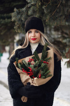 a woman holding a bouquet of flowers in her hands while walking down the street on a snowy day