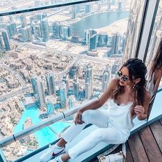 two beautiful women sitting on top of a building looking out at the city from above