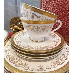 a stack of white and gold plates with golden trimmings on them, sitting next to a red box