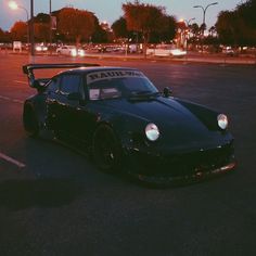 a black sports car parked in a parking lot with its hood up and lights on