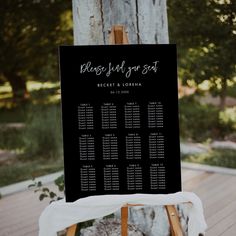 a black and white wedding seating sign sitting on top of a wooden easel next to a tree