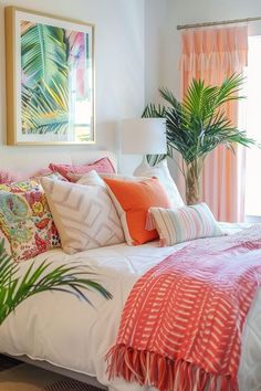 a white bed topped with lots of pillows next to a potted palm tree in front of a window