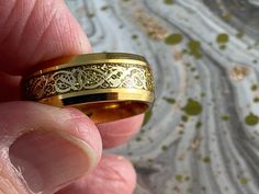 a person holding a gold ring in their hand, with an intricate design on it